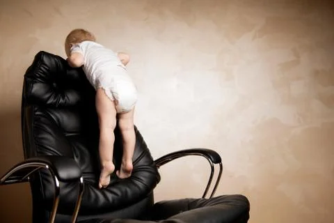 Child playing climbed onto the back of a large office chair Stock Photos