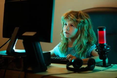 Child playing computer games or studying on pc computer. Kid gamer on night neon Stock Photos