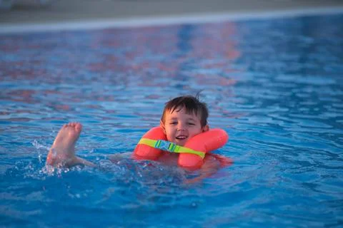 Child playing with inflatable swim ring in blue swimming pool water. Happy bo Stock Photos