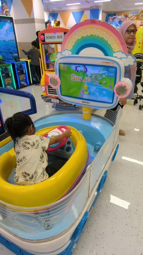 A child is playing an interactive driving game on a colorful arcade machine Stock Footage 296315440