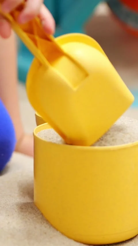 Child playing with kinetic sand using a yellow shovel and mold, pouring sand Stock-Footage 341285066