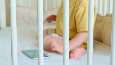 Child playing with mobile phone inside a white crib. Little boy using digital Stock Footage 344905808