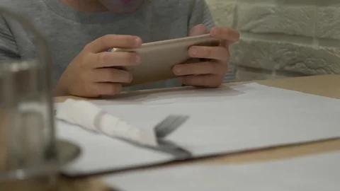 A child is playing with a mobile phone on the table, waiting for an order in a Video stock 83233425
