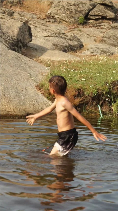 Child playing in a river while bathing and throwing dirt Stock Footage 277453937