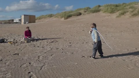 Child playing with a rope on the beach while mother watches Stock Footage 310192151