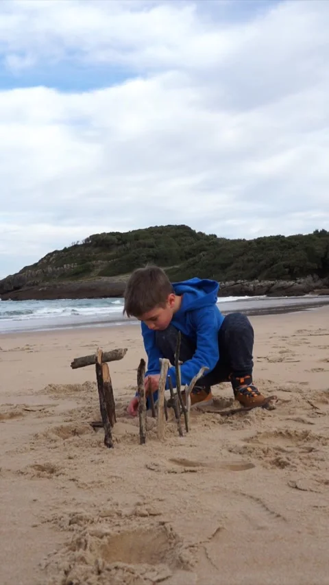 Child playing in the sand on the beach to build with some sticks in winter Stock Footage 260798577