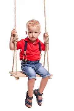 Child playing on a swing while wearing a red shirt and denim shorts in a bright Stock Photos