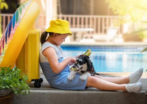 Child  playing tablet on the side of the pool with a dog and a suitcase Stock Photos