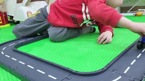 Child playing with toy car on plastic road track. Little boy sitting on green Stock Footage 341105409