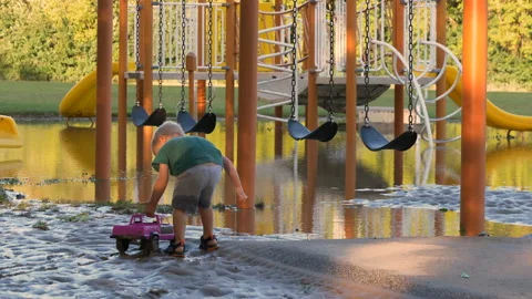 Child playing with toy truck in mud on flooded playground Vidéo 115998317