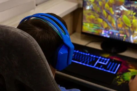Child playing video games on computer at home, wearing blue headphones. Gam.. Stock Photos