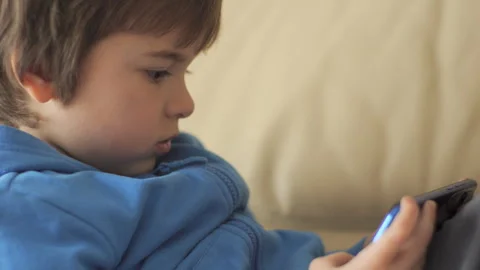 Child Playing Video Games In Mobile Phone at Home Sitting on Couch. Mobile .. 库存影片 335592360