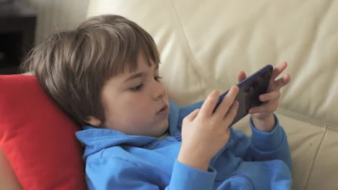 Child Playing Video Games In Mobile Phone at Home Lying on Couch. Mobile ph.. 库存影片 335592386