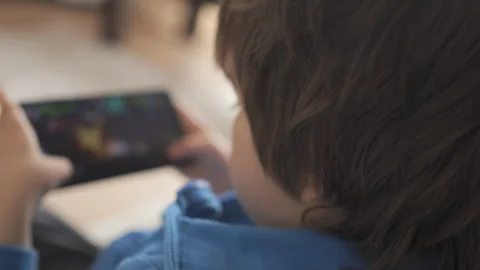 Child Playing Video Games In Mobile Phone at Home Sitting on Couch. Mobile .. 库存影片 335597232