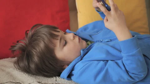 Child Playing Video Games In Mobile Phone at Home Lying on Couch. Mobile ph.. Stock Footage 335597323