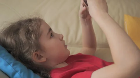 Child Playing Video Games In Mobile Phone at Home Lying on Couch. Mobile ph.. 库存影片 335599200