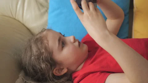 Child Playing Video Games In Mobile Phone at Home Lying on Couch. Mobile ph.. 库存影片 335599239
