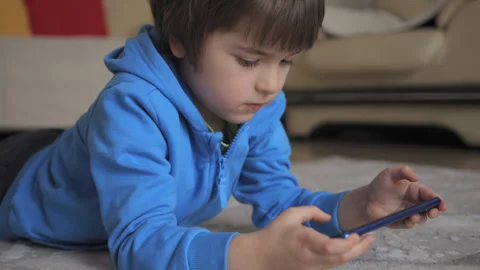 Child Playing Video Games In Mobile Phone at Home Lying on Floor. Mobile ph.. Video stock 335634141
