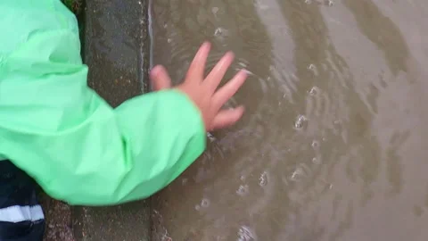 Child playing with water in a muddy puddle after rain. Kid hand touching ripple Stock Footage 341105557