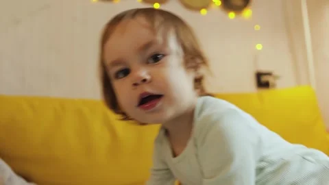 Child playing on yellow sofa and looking at camera in cozy room full of comfort Stock Footage 311246910