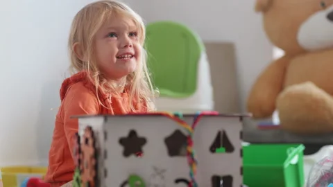 Child plays with busy cube on the floor of nursury room, huge bear on background Stock Footage 234731222