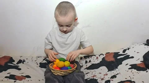 Child plays with colorful eggs while sitting on a couch in a room during the day Stock Footage 328439374