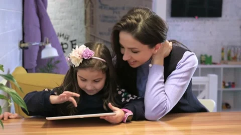 The child plays a digital tablet, mom smiles and hugs her. Stock Footage 133305809