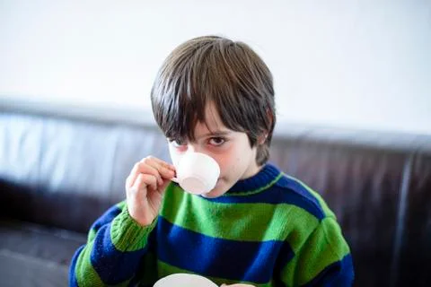 Child plays, drinking tea on the sofa Stock Photos