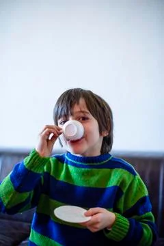 Child plays, drinking tea on the sofa Stock Photos