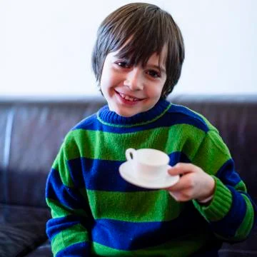 Child plays, drinking tea on the sofa Stock Photos