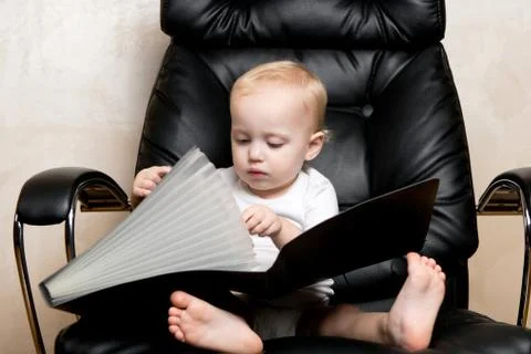 Child plays with a folder for documents, sitting in a large office chair Stock Photos