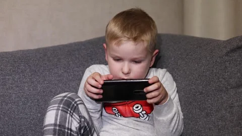 Child plays game on mobile device while sitting on couch at home during Stock Footage 322629453