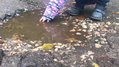 The child plays with his hands in a puddle. Rainy weather games outside Stock Footage 215738081