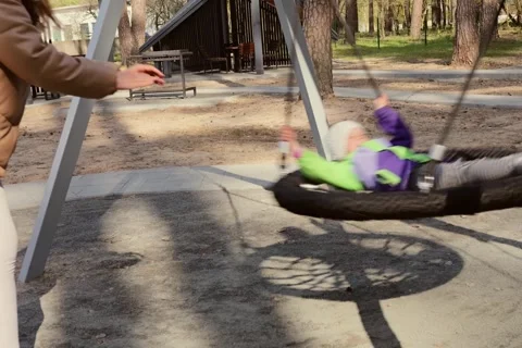 A child plays on a large swing inside a park. Another person extends a hand to Stock Footage 336464807