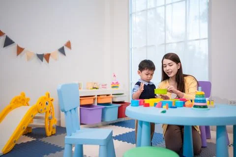 Child plays with learning toys while adult guides activity in a bright play.. Stock Photos