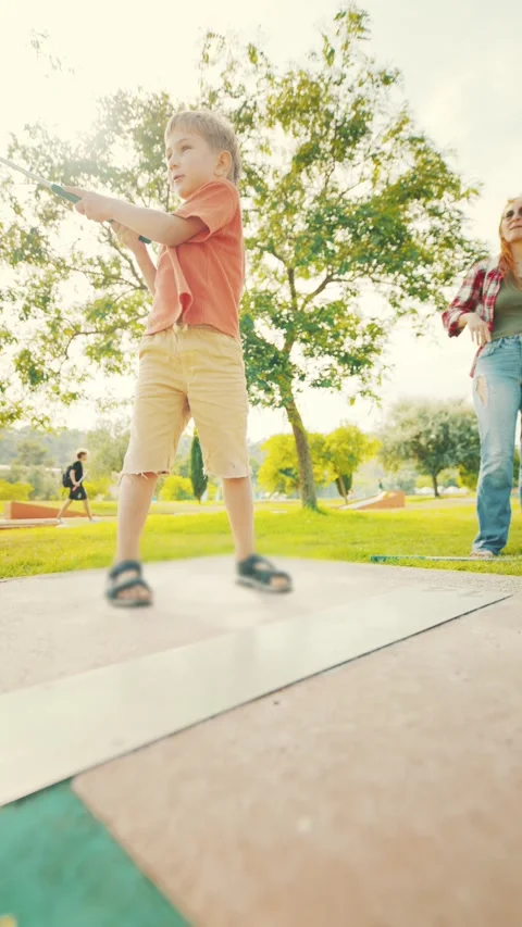 Child plays mini golf in sunny park while parent watches closely during Stock Footage 339461902
