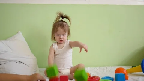 Child plays with multicolored cubes on a white bed and throws them to his mother Stock Footage 119630556