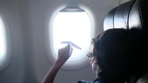 Child plays with a paper airplane inside an airplane looking out the window Stock Footage 252036726