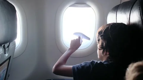 Child plays with a paper airplane inside an airplane looking out the window Stock Footage 252036727