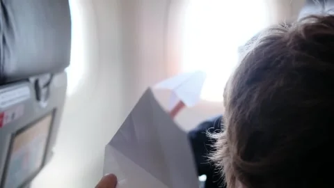 Child plays with a paper airplane inside an airplane looking out the window Stock Footage 252036845