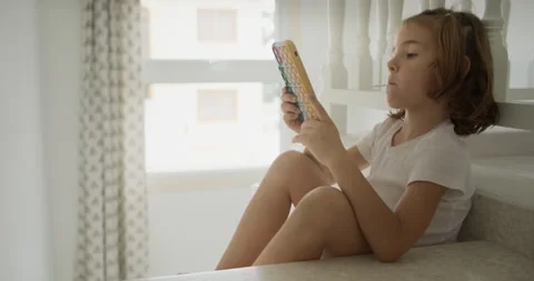 A child plays with the phone alone while sitting on the stairs. Vídeos de archivo 243339591