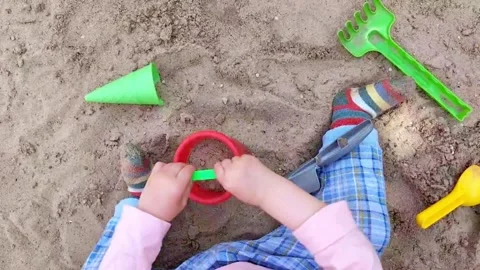 A child plays in a sandbox with a red bucket and scoop Stock Footage 276281996