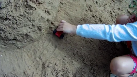 A child plays in a sandbox with a small car model Stock Footage 78047748