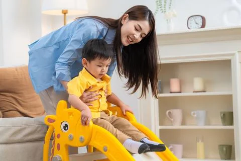 Child plays on a small slide while an adult helps him in a cozy living room.. Stock Photos