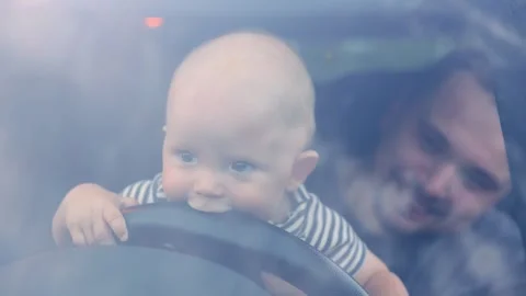 Child plays with steering wheel while father smiles in car on a sunny day Stock-Footage 308250003