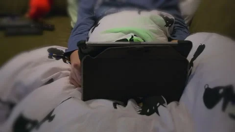 A child plays on a tablet under the covers in bed at night Stockbeeldmateriaal 323080690