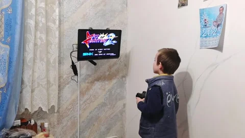 Child plays video game on screen in home with wall calendar and gaming controlle Stock Footage 327102192