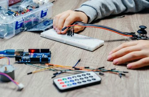 A child plugging cables to sensor chips while learning arduino coding and Stock Photos
