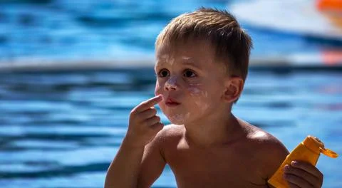 Child by the pool applying sunscreen. Stock Photos