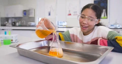 Child pouring orange from beaker into flask in lab demo, causing foam overflow, Stock Footage 340676295